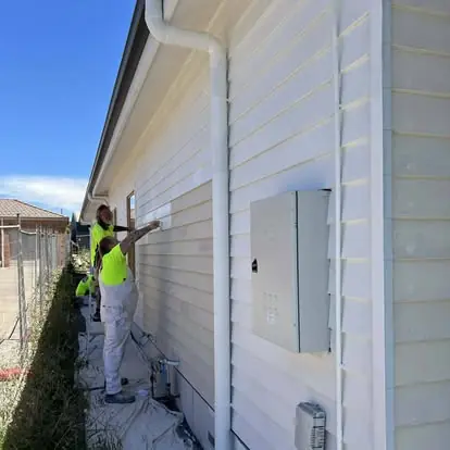 Painter applying white paint to exterior weatherboard siding
