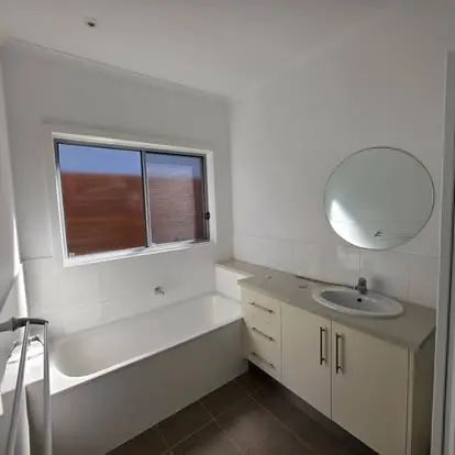 Finished bathroom with white bath, timber vanity and round mirror