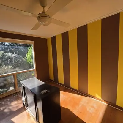 Feature wall with alternating yellow and dark vertical stripes in a sunlit room