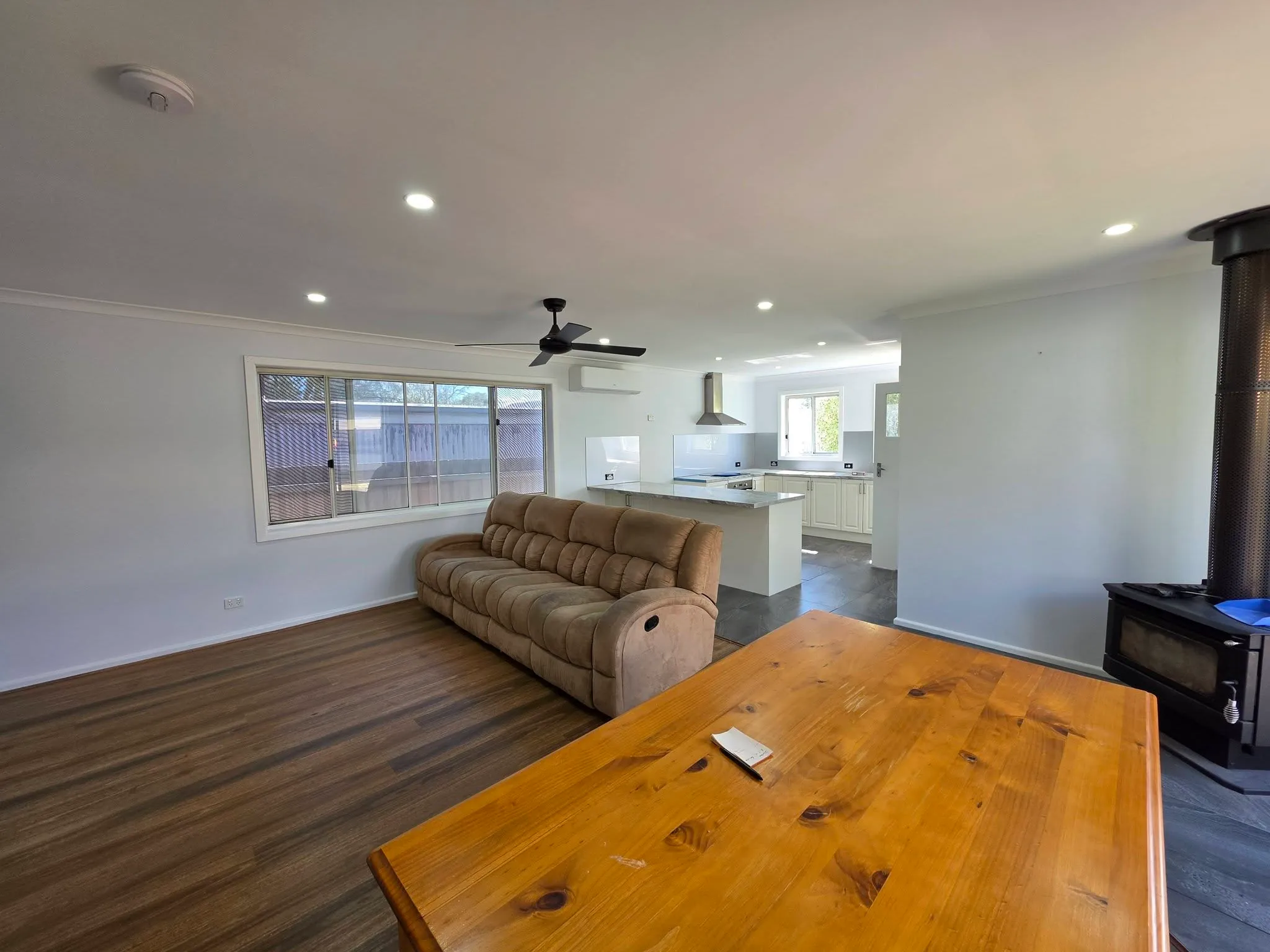 Freshly painted open-plan living room with white walls, timber flooring and kitchen beyond