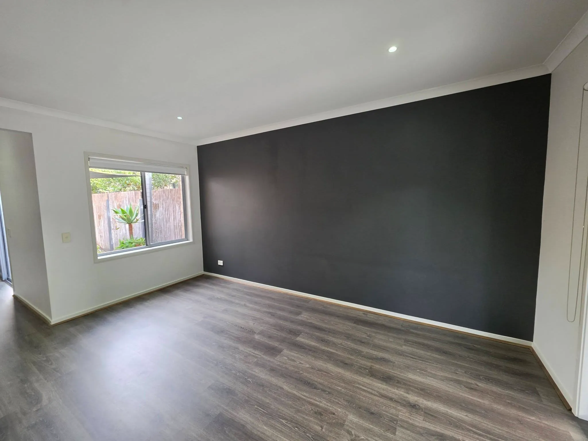 Empty room with a charcoal feature wall, downlights and timber-look flooring